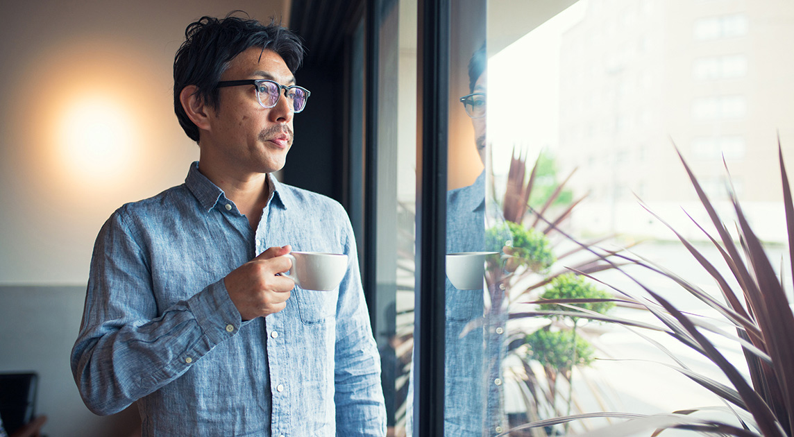 Covered California member looks out the window while drinking coffee.