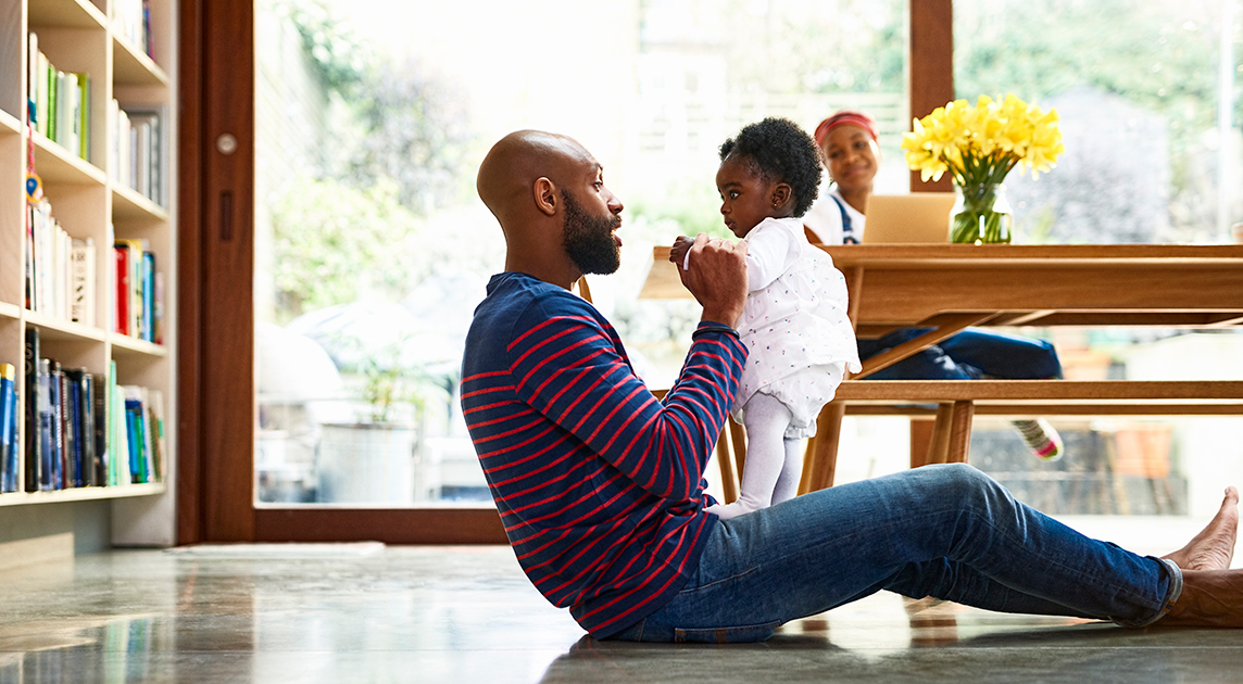 A Covered California member who has saved money on health insurance through the American Rescue Plan plays in his living room with is baby and wife. 
