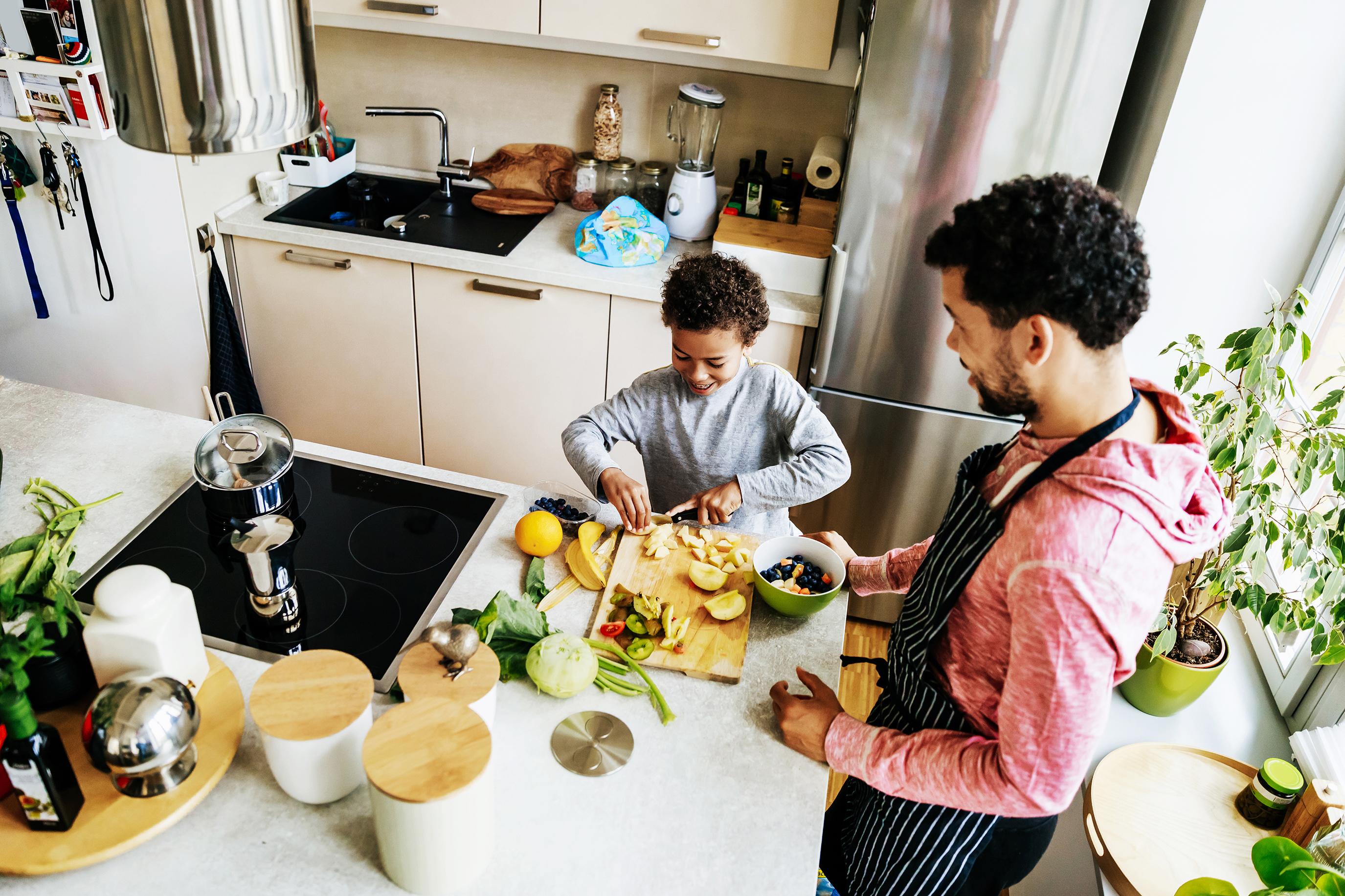 A dad.......... and his son make a healthy meal together at home.